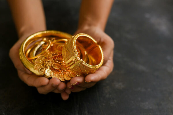 Hände halten goldene Armbänder und Goldmünzen, die zum Goldankauf angeboten werden.