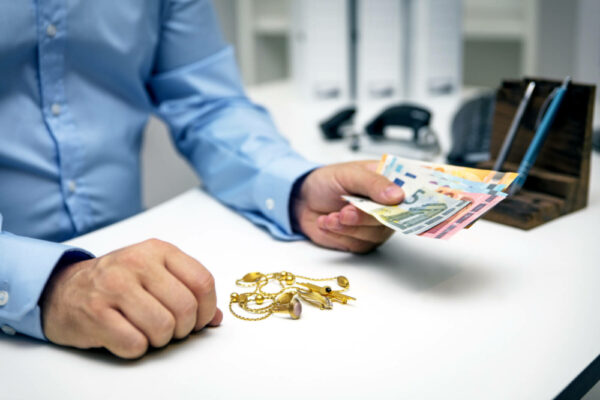 Goldschmuck verkaufen: Person sitzt am Schreibtisch und tauscht Bargeld gegen Goldschmuck aus.